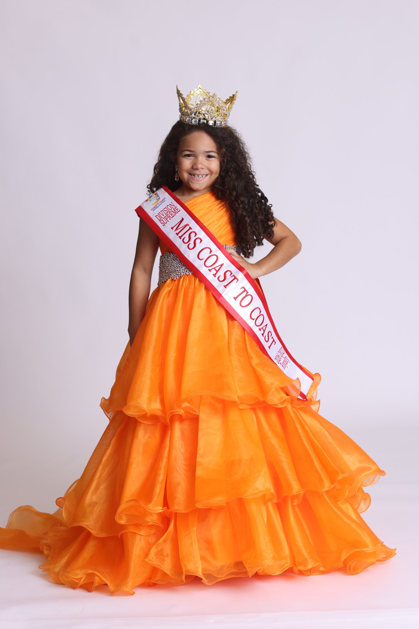 Crowned contestant in an orange evening gown and sash